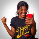 A cheerful woman celebrates success while looking at her smartphone, expressing happiness.